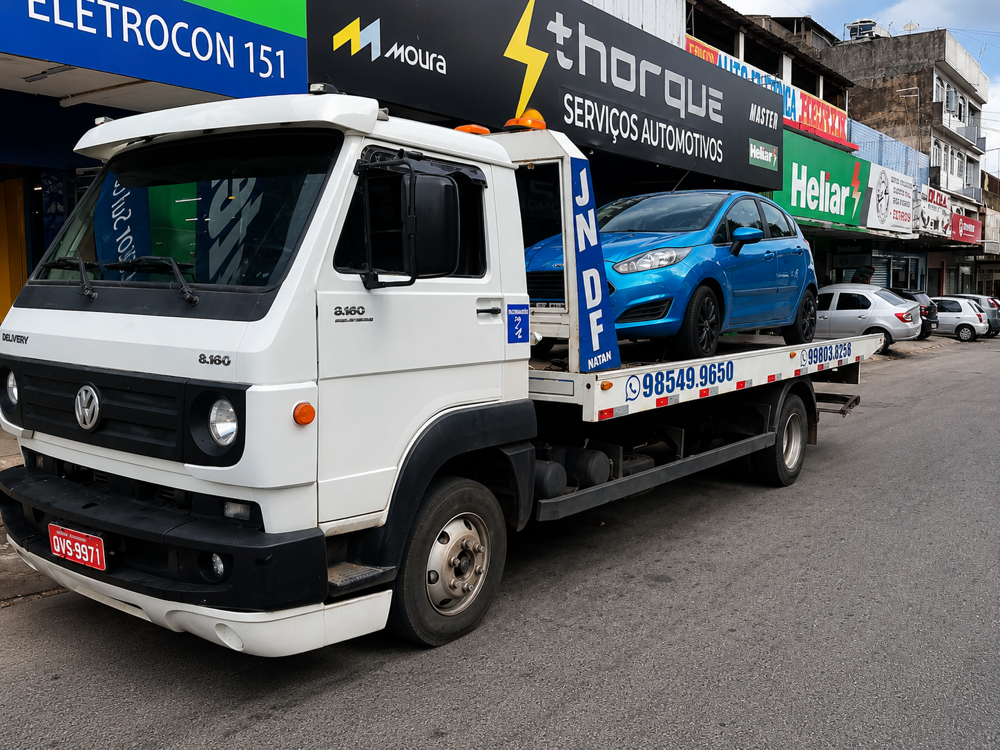 Caminhão guincho da JN DF Guincho transportando um carro azul em frente a uma loja de serviços automotivos